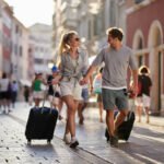 Happy couple of tourists talking while dragging their suitcases on the street.