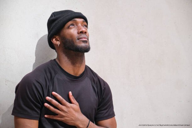 LE POUVOIR DE LA GRATITUDE : CE QUE DIT LA SCIENCE SUR LE BIEN-ÊTRE 6 Young black man standing with hand over heart while looking up with hope