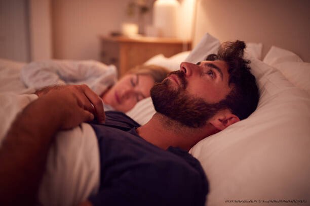 CES SYMPTÔMES PHYSIQUES QUI CACHENT EN RÉALITÉ UNE DÉPRESSION QUE VOUS N'AVEZ PAS DÉTECTÉE 4 Couple With Man Lying In Bed Awake At Night Suffering With Insomnia