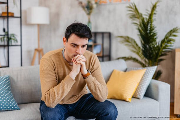 COMMENT RETOMBER À NOUVEAU AMOUREUX(E) APRÈS UNE DÉCEPTION SENTIMENTALE DOULOUREUSE EN 5 ÉTAPES 6 Sad young man sitting on the sofa at home.