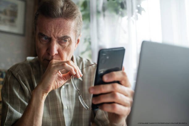 COMMENT DES CRIMINELS UTILISENT L'IA POUR CRÉER DES ARNAQUES IMPOSSIBLES À DÉTECTER 4 Senior man looking seriously at smartphone