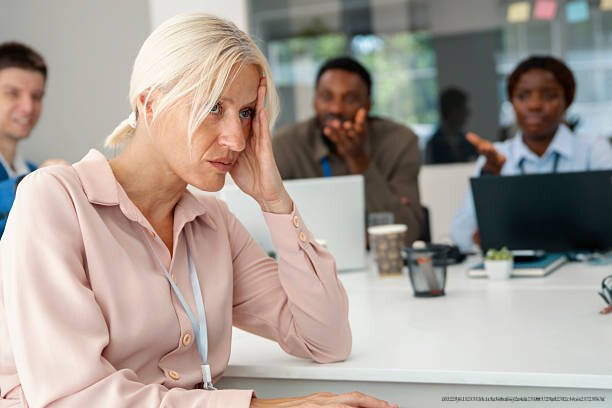 COMMENT NOTRE CERVEAU CRÉE DES PRÉJUGÉS SANS QUE NOUS LE SACHIONS JAMAIS 4 Colleagues gossiping with sad businesswoman in foreground