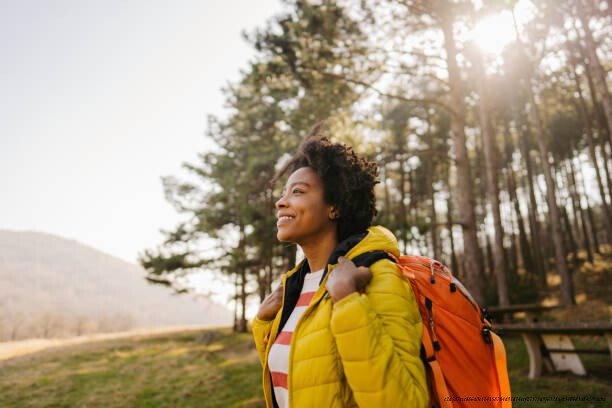 LES BIENFAITS DE LA NATURE SUR LA SANTÉ MENTALE 6 Photo of a young smiling woman carrying a backpack and hiking in the nature