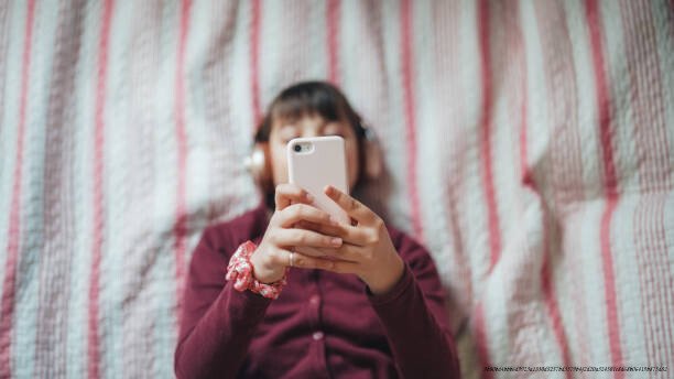 APPLICATIONS SECRÈTES ET DANGEREUSES POUR LES ENFANTS : CE QUE VOUS DEVEZ SAVOIR 6 Girl in bed enjoying a good music from smartphone app