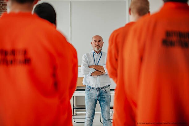 DES DÉTENUS QUI ONT TRANSFORMÉ LEUR CELLULE EN LIEUX D'APPRENTISSAGE ET DE CRÉATION 6 In a bright classroom, a dedicated teacher guides a multiracial group of male prisoners focused on their studies.