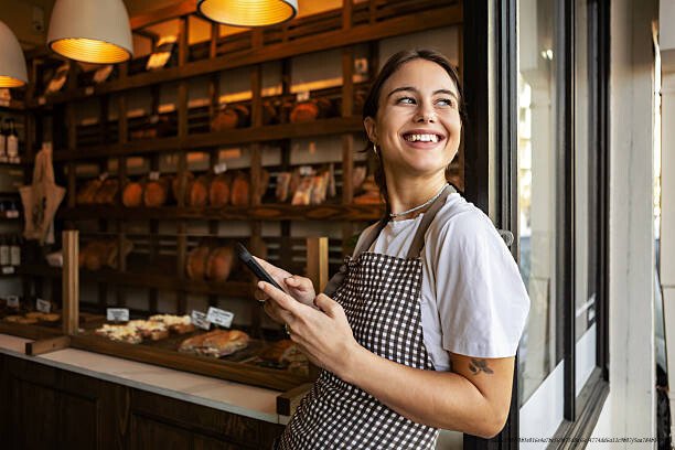 L'ASCENSION DES EX-DÉTENUS EN TANT QU' ENTREPRENEURS BRILLANTS 6 Smiling young female baker standing proudly in front of bakery using phone