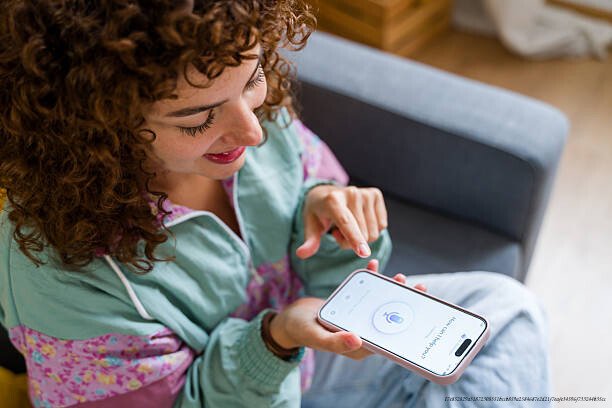 APPRENDRE UNE LANGUE EN 6 MOIS : LES APPLICATIONS RÉVOLUTIONNAIRES 4 Young woman using voice assistant app on smartphone for smart home control
