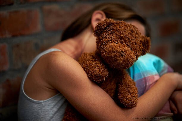 LA PSYCHOLOGIE DE LA VICTIME : COMPRENDRE LES MÉCANISMES ET FACTEURS D'EXPOSITION 6 Abused little girl holding a teddy bear tightly while huddled over