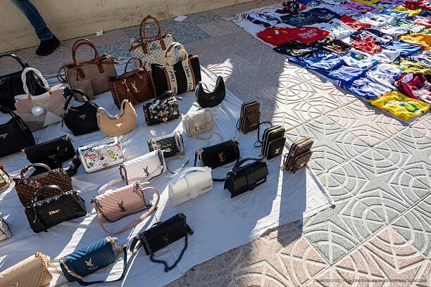 L'IMPACT ÉCONOMIQUE DES CONTREFAÇONS DE LUXE ET LEURS LIENS AVEC LE CRIME ORGANISÉ 5 Handbags and shirts displaying fake luxury brands for sale at an outdoor market